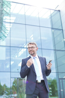 Geschäftsmann im Freien mit Mobiltelefon und Kopfhörern - MAEF011790