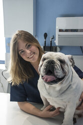 Portrait of smiling veterinarian with dog in a veterinary clinic - ABZF000630