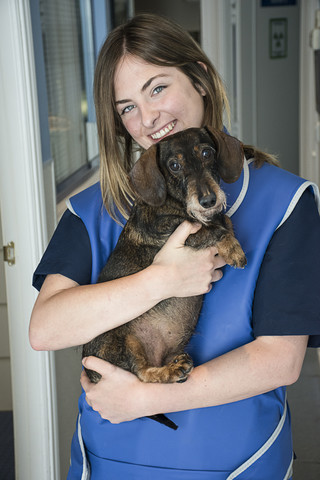 Porträt einer lächelnden Tierärztin, die einen Hund in ihren Armen hält, lizenzfreies Stockfoto