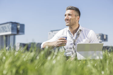 Germany, Cologne, smiling businessman with digital tablet in meadow - MADF000909