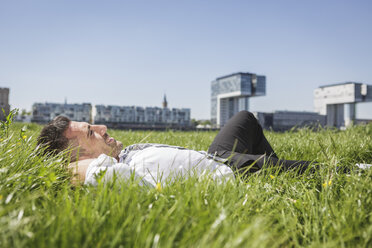Germany, Cologne, smiling businessman lying in meadow - MADF000911
