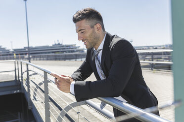 Smiling businessman with cell phone at the airport - MADF000933