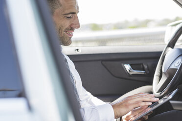 Lächelnder Geschäftsmann benutzt digitales Tablet im Auto - MADF000950