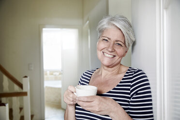 Porträt einer lächelnden Frau mit einer Tasse Kaffee zu Hause - FMKF002724