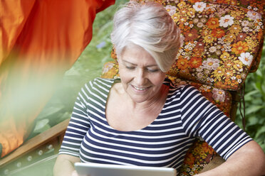 Woman sitting in lawn chair using digital tablet - FMKF002747