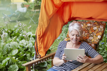 Woman sitting in lawn chair using digital tablet - FMKF002748