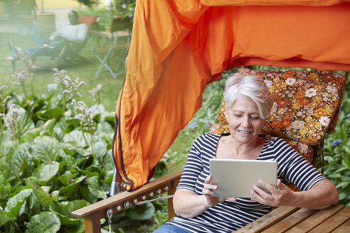 Frau sitzt im Liegestuhl und benutzt ein digitales Tablet - FMKF002748