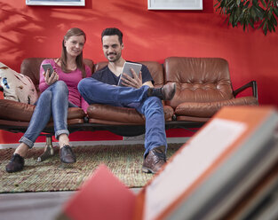Junger Geschäftsmann und Frau sitzen auf einer alten Couch und benutzen digitale Geräte - RHF001502