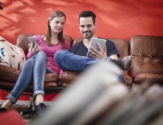 Junger Geschäftsmann und Frau sitzen auf einer alten Couch und benutzen digitale Geräte - RHF001503