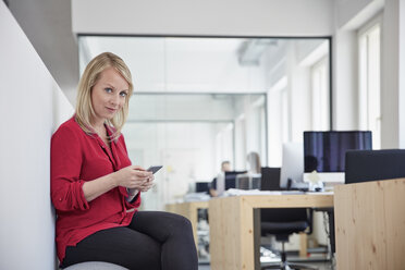 Frau sitzt im Büro und benutzt ein Smartphone - RHF001520