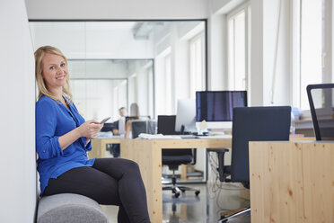 Frau sitzt im Büro und benutzt ein Smartphone - RHF001522