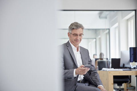 Älterer Geschäftsmann im Büro mit Smartphone, lizenzfreies Stockfoto