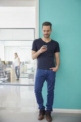 Man standing in office using smart phone - RHF001533