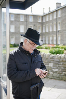 UK, Bristol, senior man using smartphone while waiting at bus stop - JCF000007