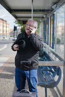 UK, Bristol, portrait of laughing senior man telephoning with smartphone while waiting at bus stop - JCF000008