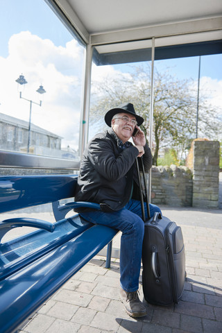 UK, Bristol, Porträt eines lächelnden älteren Mannes, der mit seinem Smartphone telefoniert, während er an der Bushaltestelle wartet, lizenzfreies Stockfoto