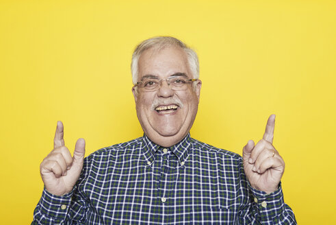 Portrait of laughing senior man gesturing in front of yellow background - JCF000030