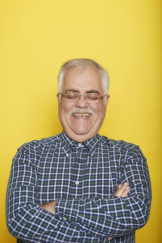 Porträt eines lächelnden älteren Mannes mit verschränkten Armen und geschlossenen Augen vor einem gelben Hintergrund, lizenzfreies Stockfoto