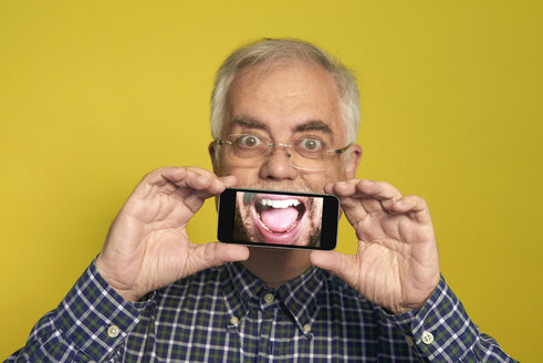 Portrait of senior man holding smartphone with photography of open mouth - JCF000032