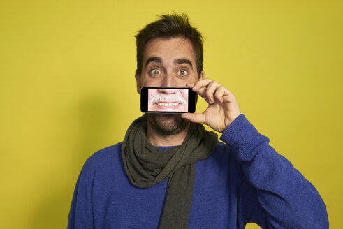 Portrait of man holding smartphone with photography of another man's smiling mouth - JCF000033