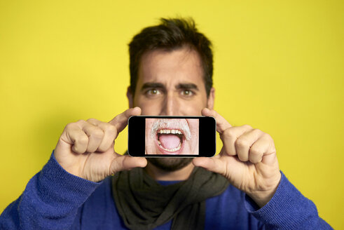 Portrait of man holding smartphone with photography of another man's screaming mouth - JCF000034