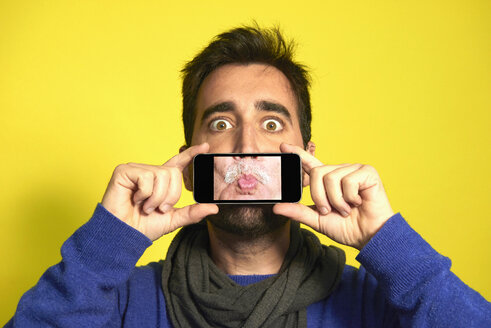 Portrait of man holding smartphone with photography of another man's pout - JCF000035