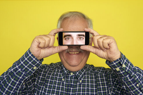 Porträt eines lächelnden älteren Mannes, der ein Smartphone mit einer Fotografie der Augen eines anderen Mannes hält - JCF000036