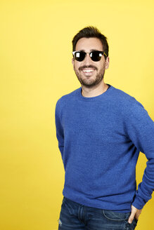 Portrait of smiling man wearing sunglasses in front of yellow background - JCF000037