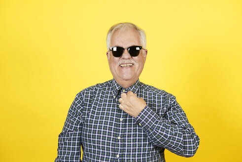 Portrait of smiling senior man wearing sunglasses in front of yellow background - JCF000038