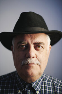 Portrait of serious senior man wearing black hat in front of grey background - JCF000043