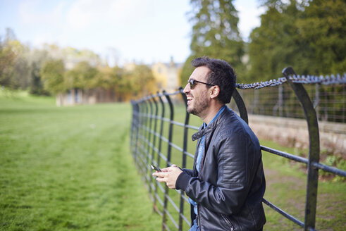 Lachender Mann mit Smartphone in Lederjacke und Sonnenbrille - JCF000050