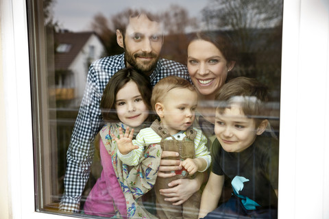 Happy family of five looking through window pane stock photo