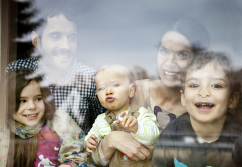 Glückliche fünfköpfige Familie schaut durch eine Fensterscheibe, lizenzfreies Stockfoto