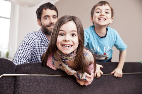 Porträt eines grinsenden kleinen Mädchens zu Hause mit Vater und Bruder im Hintergrund, lizenzfreies Stockfoto