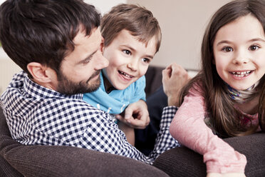 Junge und Mädchen kuscheln mit ihrem Vater auf der Couch zu Hause - MFF002979