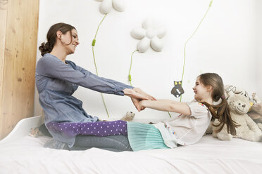 Mother playing with her little daughter on bed - MFF002988