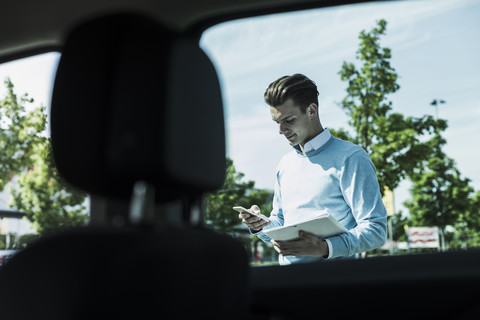 Junger Mann mit Mobiltelefon vor Auto, lizenzfreies Stockfoto