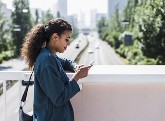 Young woman on bridge looking at cell phone - UUF007490