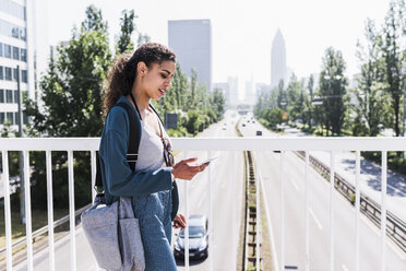 Junge Frau auf Brücke schaut auf Handy - UUF007491