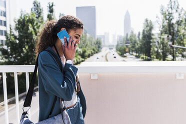 Junge Frau auf einer Brücke, die mit einem Handy telefoniert - UUF007492