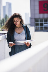 Young woman with cell phone and document outdoors - UUF007499