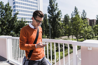 Young man on bridge looking at cell phone - UUF007507