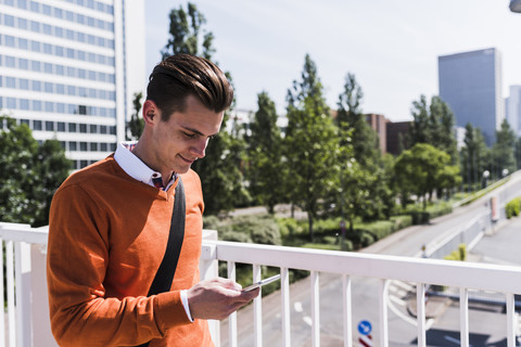 Junger Mann auf Brücke schaut auf Handy, lizenzfreies Stockfoto