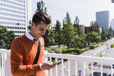 Young man on bridge looking at cell phone - UUF007508