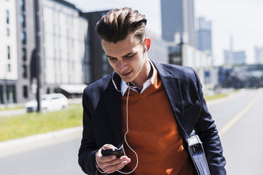 Young man with cell phone and earbuds on the move - UUF007524