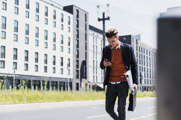 Young man with cell phone and earbuds on the move - UUF007525