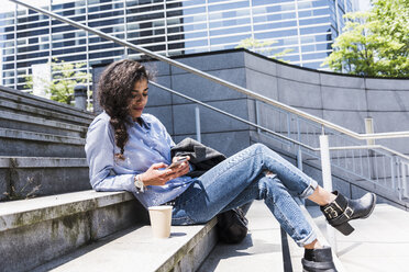 Young woman sitting on stairs looking at cell phone - UUF007532