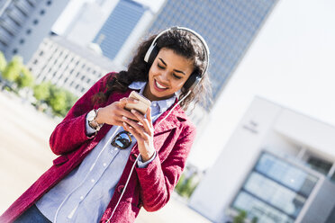 Smiling young woman with cell phone wearing headphones - UUF007543