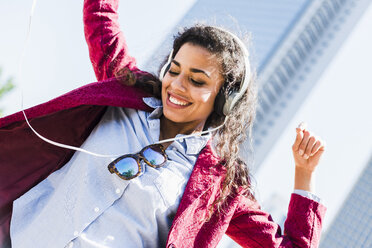 Happy young woman with headphones moving outdoors - UUF007544