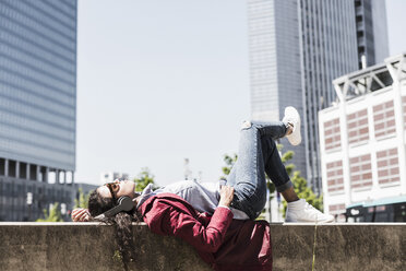 Relaxed young woman wearing headphones lying on wall - UUF007548